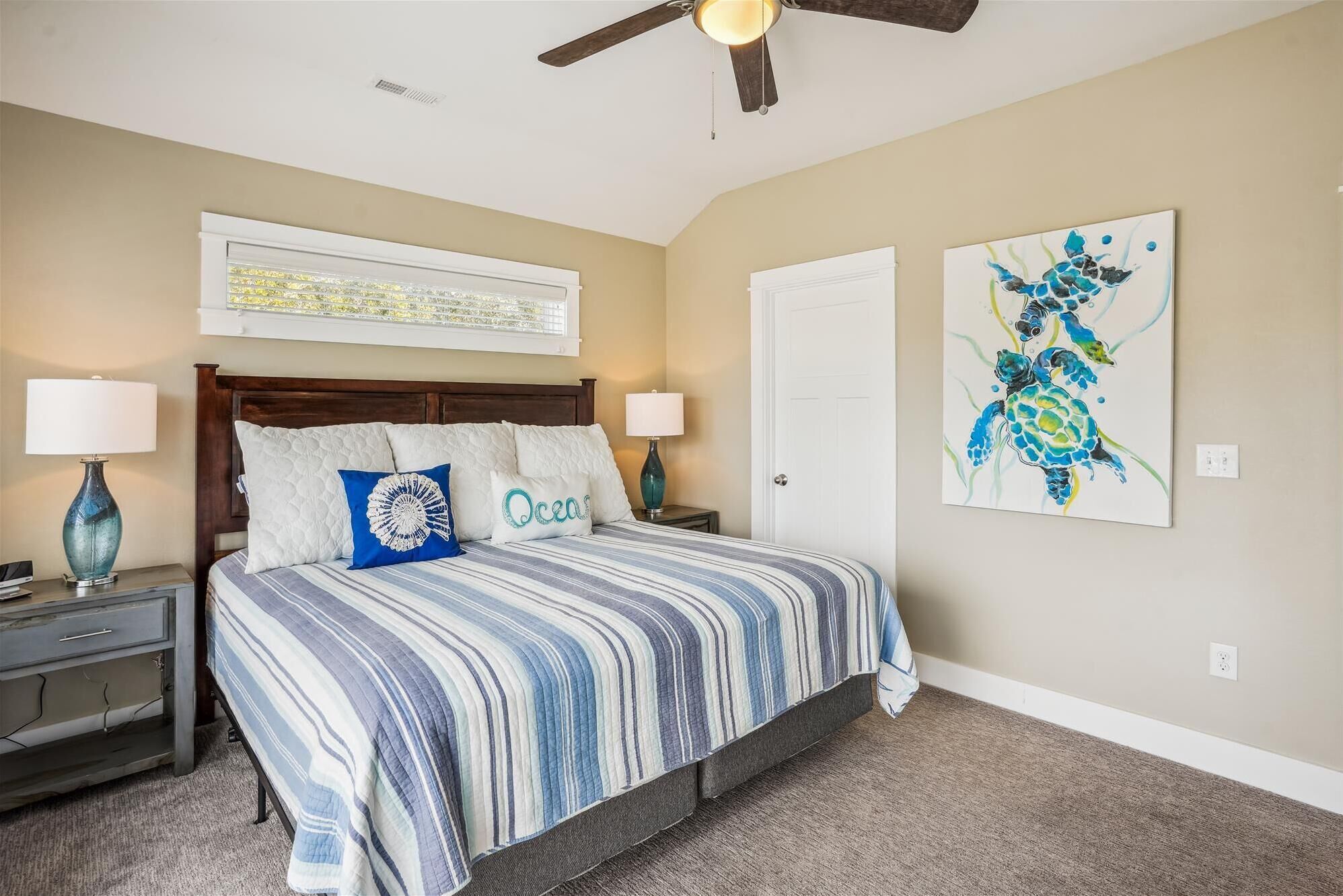A bedroom with a large bed, two bedside tables, a ceiling fan, and artwork on the walls.