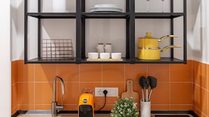 A kitchen with a black metal shelf unit above a tiled backsplash, containing white dishes, a yellow pot, and a wine glass. - Ghiberti - Lovely nest in the city (Trieste)