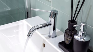 A bathroom sink with a chrome faucet, a black soap dispenser, and a black container holding black reeds. - Ghiberti - Lovely nest in the city (Trieste)