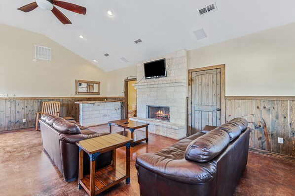 A spacious living room with a stone fireplace, leather sofas, and a wooden coffee table. - In Concan | Private Pool | Huge Outdoor Space (Concan)