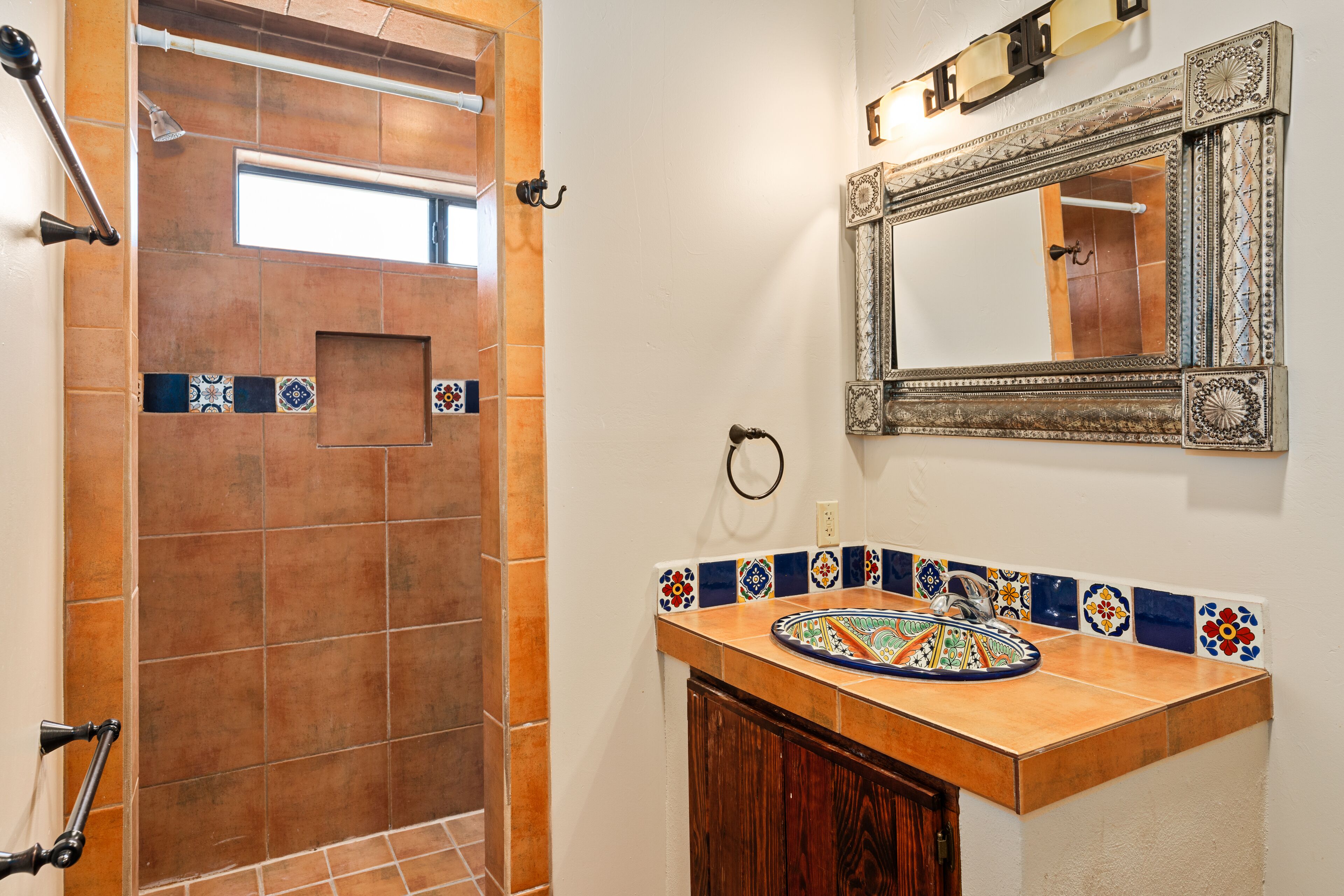A bathroom with a shower area, a sink with a decorative tile backsplash, and a mirror with an ornate frame.