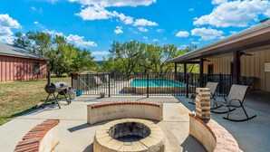 Un jardin avec un barbecue, un foyer extérieur, une piscine et un espace salon aménagé.