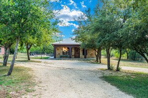 A small stone building with a covered porch, surrounded by trees and a gravel path. - Private Pool | In Concan | Family Fun (Concan)