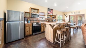 Une cuisine spacieuse dotée d’un îlot central, d’appareils électroménagers en acier inoxydable, de meubles de rangement en bois et d’un drapeau américain accroché au mur.