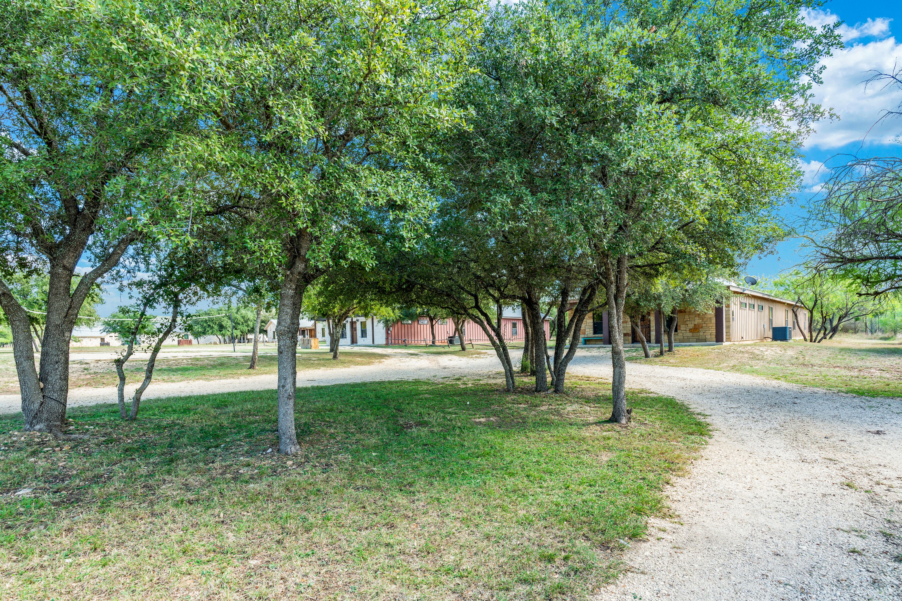 A gravel path leading to a building with a red roof, surrounded by trees and a grassy area.