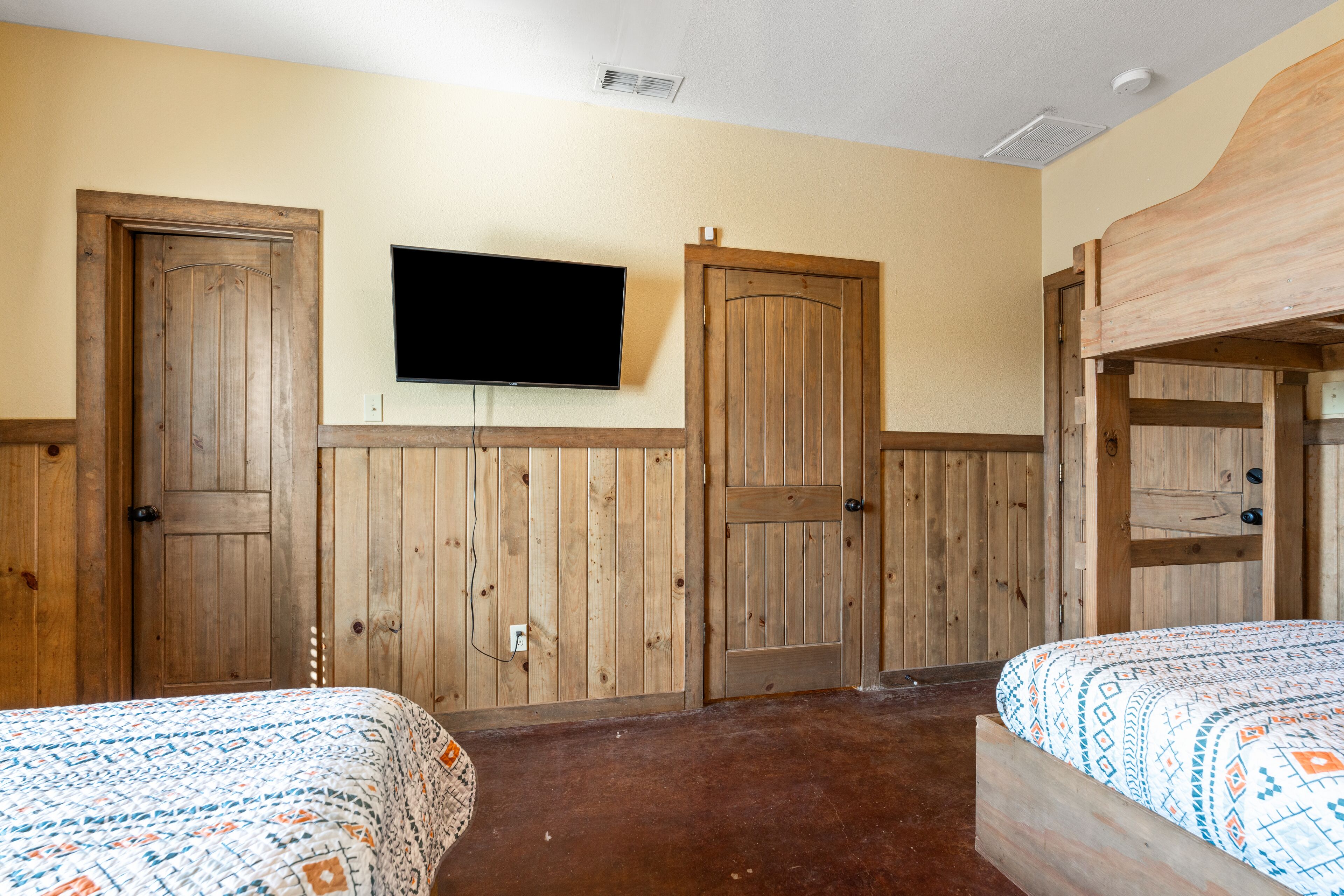 A room with two beds, wooden walls, a mounted TV, and a bunk bed.