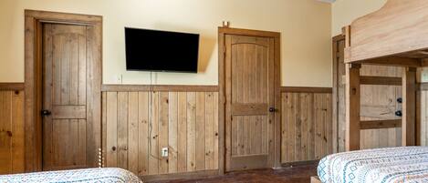 A room with two beds, wooden walls, a mounted TV, and a bunk bed.