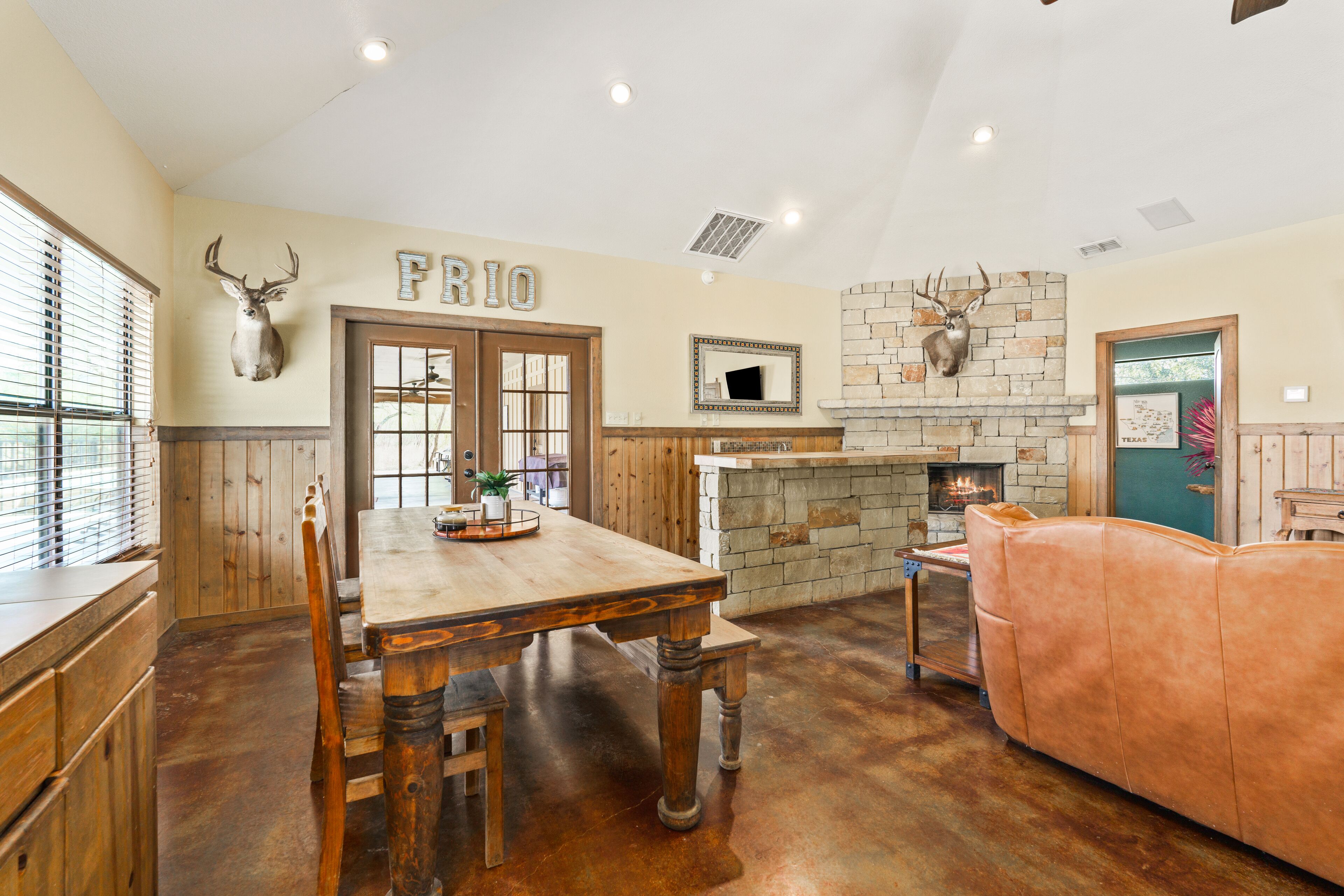 A rustic interior with a wooden dining table, a stone fireplace, and a leather couch.