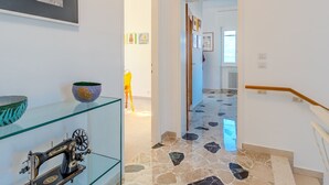 A hallway with a sewing machine on a glass shelf, a framed picture on the wall, and a tiled floor.