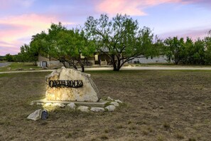 A stone sign with the name "ONTINE ROCKS" in a rural setting with trees and a building in the background.