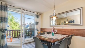Un coin repas avec une table en bois, quatre chaises, un vase de fleurs, un luminaire suspendu et un grand miroir au mur.