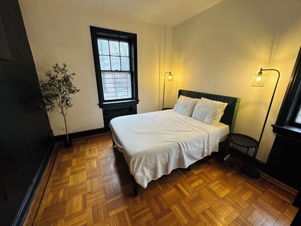 A bedroom with a wooden parquet floor, a bed with white bedding, a window with a view, and two wall-mounted lamps. - Discover Downtown Jersey City, just steps away from Liberty State Park (Jersey City)