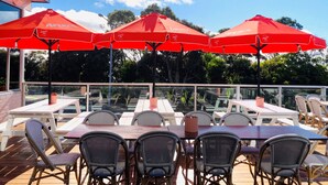 An outdoor patio with tables and chairs, red umbrellas, and a view of trees and sky. - Bridport Bay Inn (Bridport)