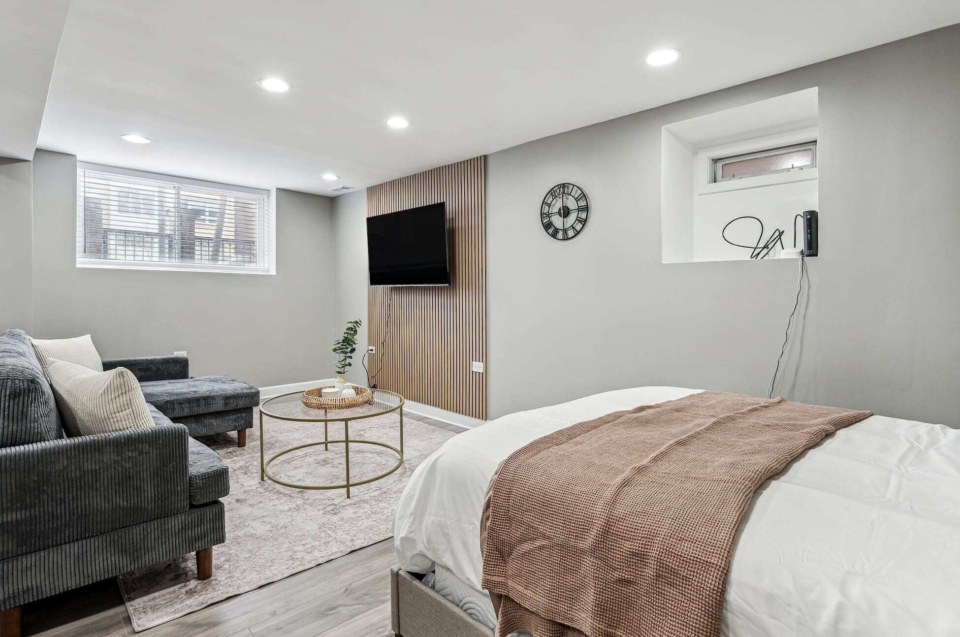 A modern bedroom with a bed, a sofa, a TV, and a clock on the wall.