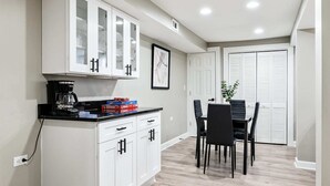A modern kitchen with white cabinets, a coffee maker, and board games on the counter.