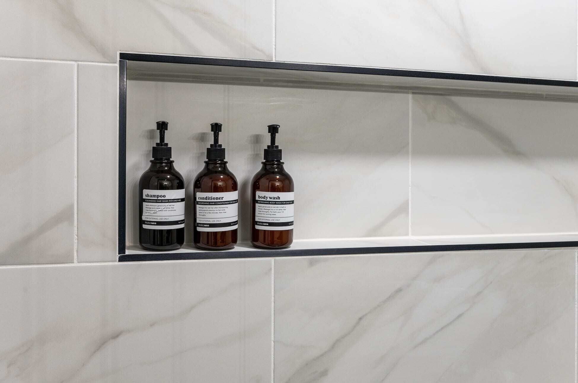A bathroom shelf with three bottles of toiletries: shampoo, conditioner, and body wash.