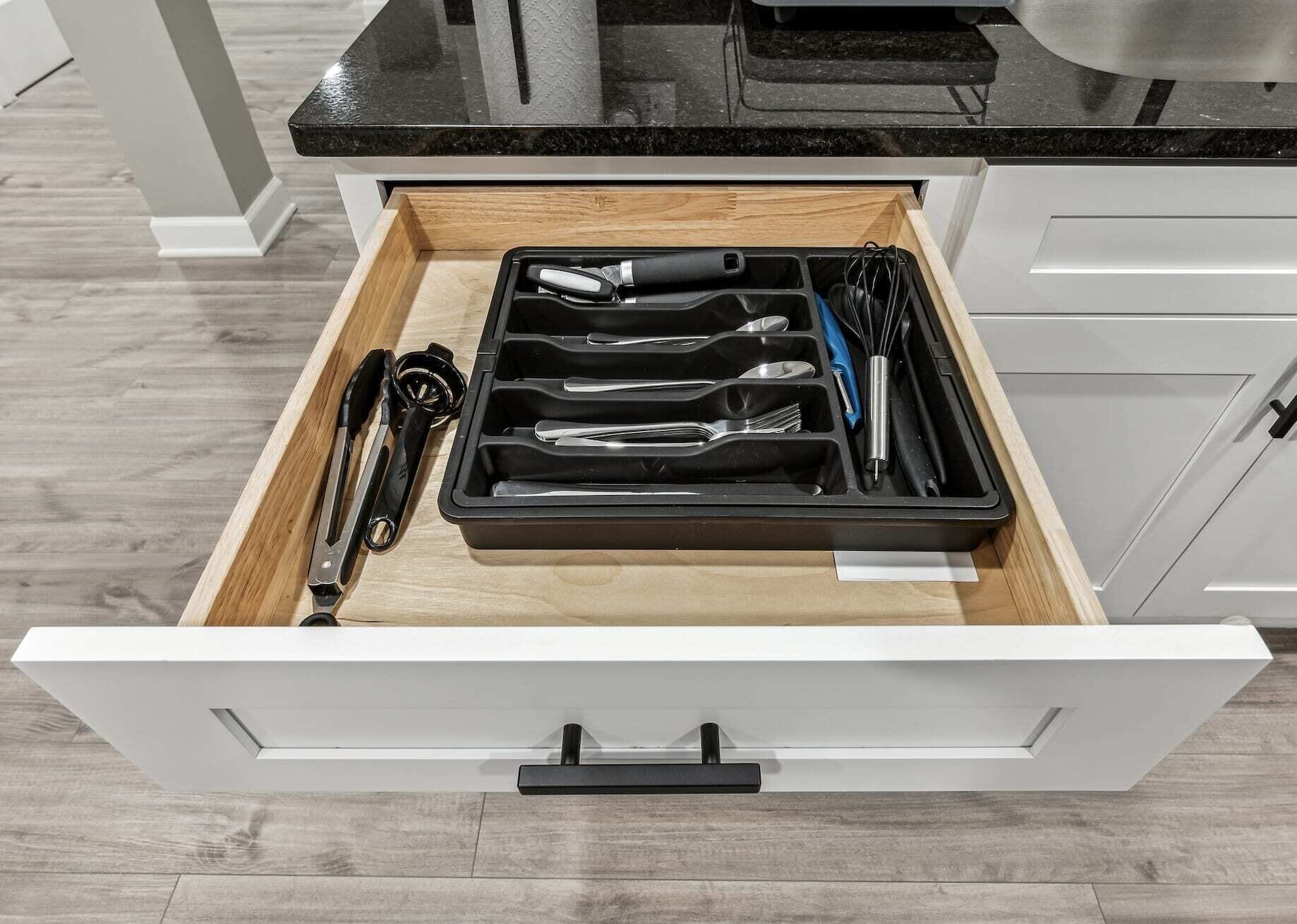 A kitchen drawer with utensils and a black tray.