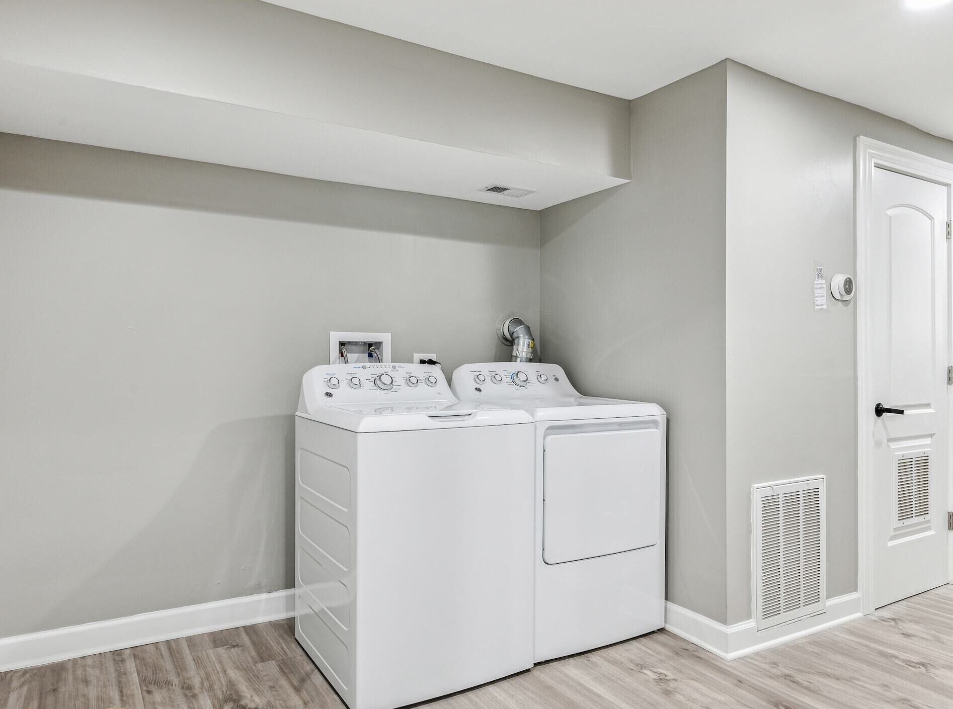 A laundry room with two stacked front-loading washers and dryers, a white door, and a vent on the wall.