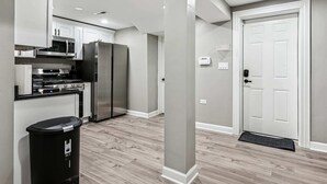 A modern kitchen with stainless steel appliances, a trash bin, and a door with a doormat.