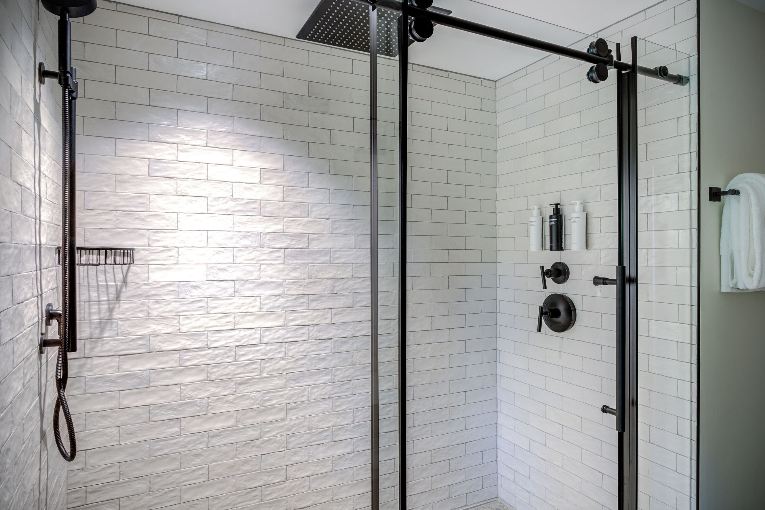 Un espace douche moderne avec une porte en verre, des murs en briques blanches et un porte-serviettes.