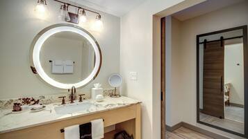 Un baño moderno con un espejo grande, un tocador redondo y una zona de ducha.