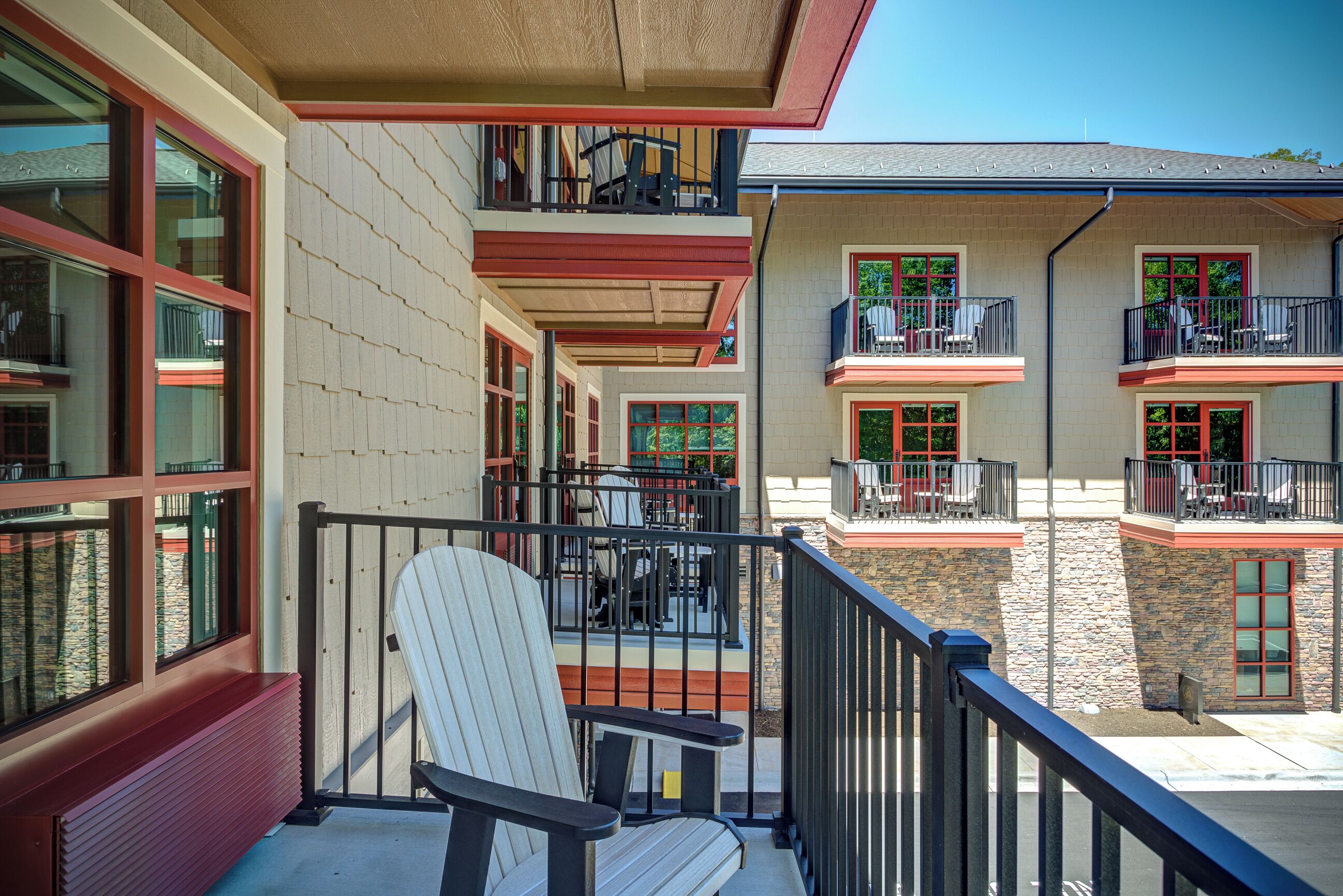 A balcony with a Adirondack chair, a stone wall, and a building with multiple balconies and windows.