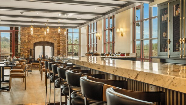 A modern bar area with a long counter, leather bar stools, and a stone fireplace.