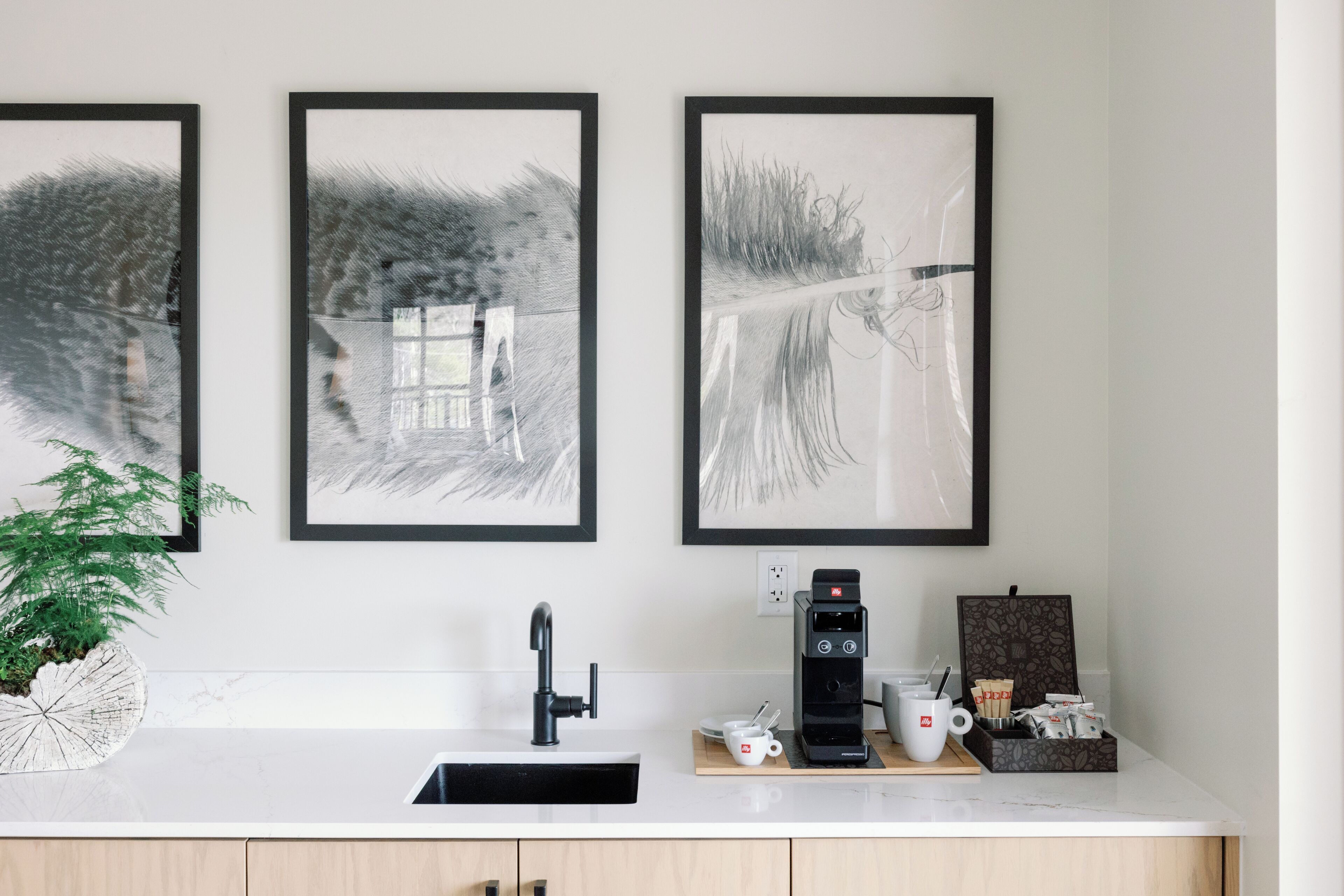 A kitchen with a white countertop, a black coffee machine, a white mug, and a plant.