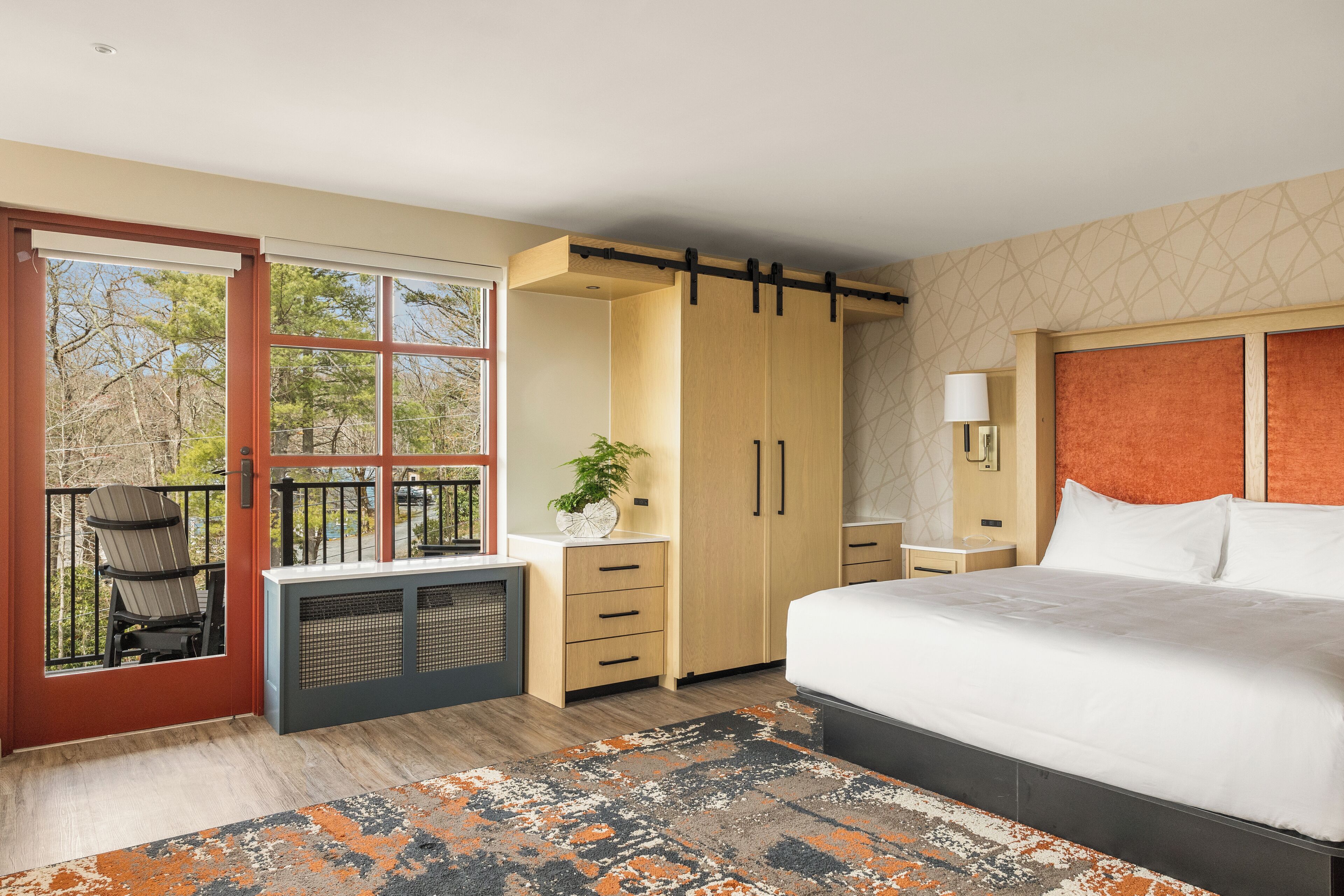 A bedroom with a large bed, a desk with a chair, a wardrobe, and a balcony with chairs.