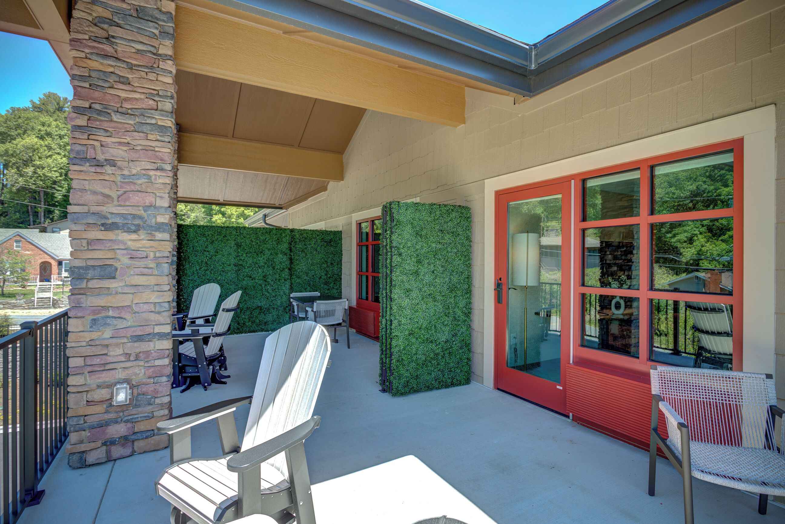 A covered patio area with outdoor seating, stone pillar, and red-framed glass doors.