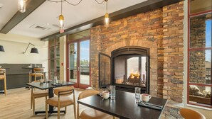 A dining area with a stone fireplace, wooden chairs, and a table with a coffee cup and glasses.
