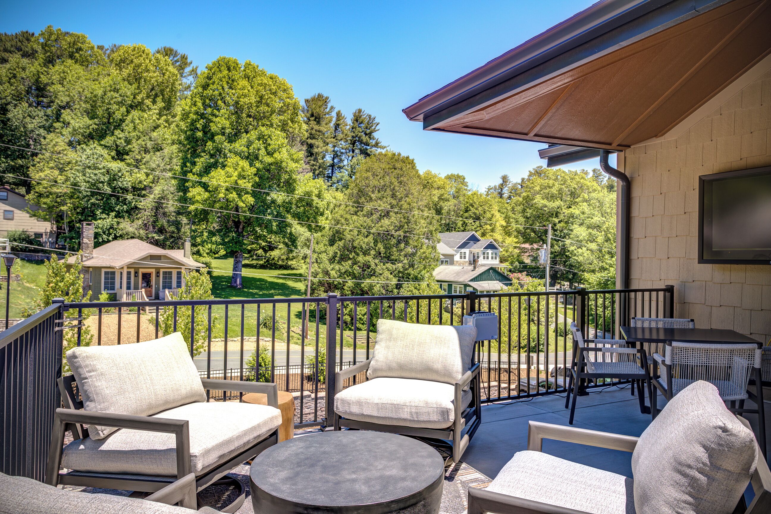A balcony with outdoor furniture, including chairs and a table, overlooking a residential area with houses and trees.