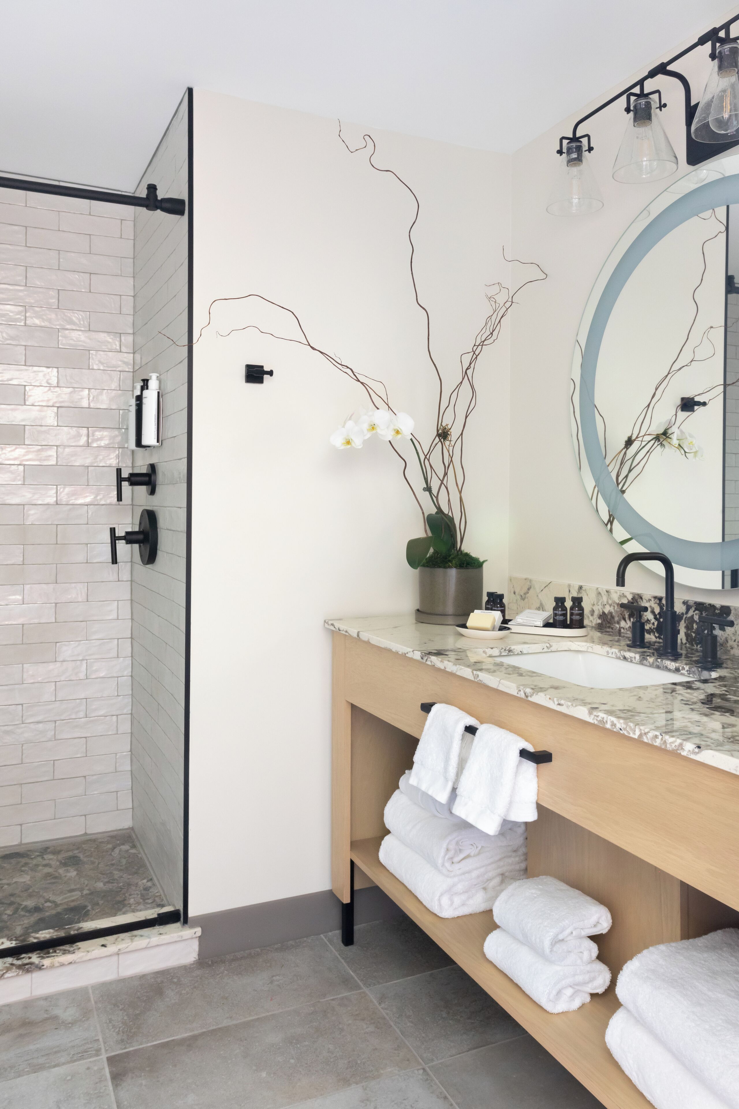 Un baño moderno con cabina de ducha de vidrio, lavabo de mármol, un espejo grande y toallas ordenadas en una repisa.