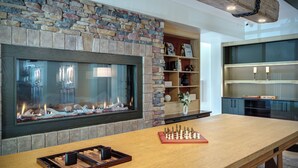 A spacious room with a stone fireplace, a wooden table with a chessboard, and a cozy shelving unit.
