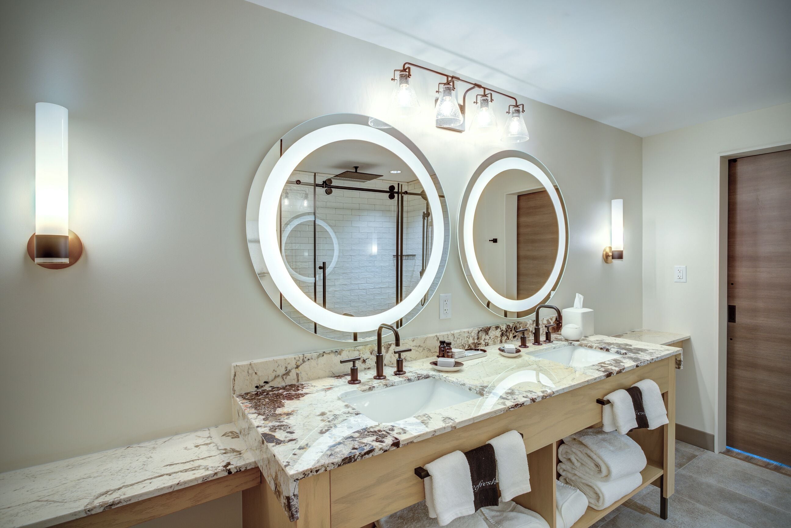 A modern bathroom with two sinks, large mirrors, and a vanity with towels.