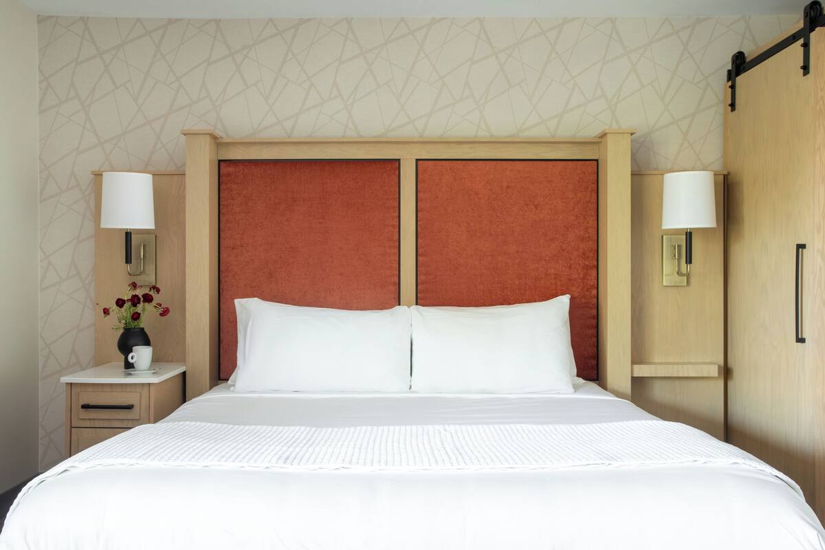 A hotel room with a large bed, two nightstands, a wooden wardrobe, and a wall with a geometric pattern.