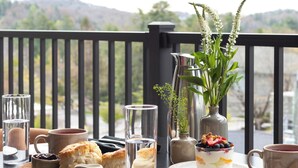 Una mesa de comedor dispuesta con un postre, bebidas y vistas al exterior.