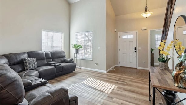 A spacious living room with a large L-shaped sectional sofa, a dining table with chairs, and a staircase leading to another level. - Homestead Haven | Sleeps 14 | 2 Car Garage (Clearfield)
