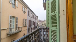 A narrow street with buildings on either side, a balcony with ornate metal railings, and a green door.