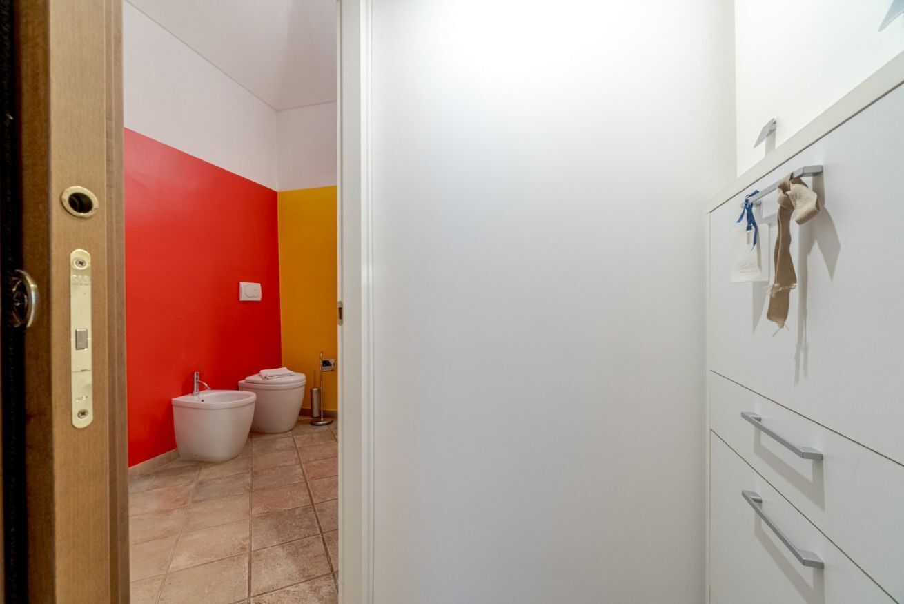 A bathroom with a red and yellow wall, a white sink, and a white cabinet with drawers.
