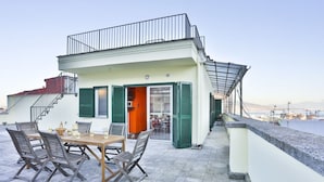 A rooftop terrace with a table and chairs, a balcony with a railing, and a view of the sea. - GuestHost - Terrace Concordia Amazing View (Napoli)