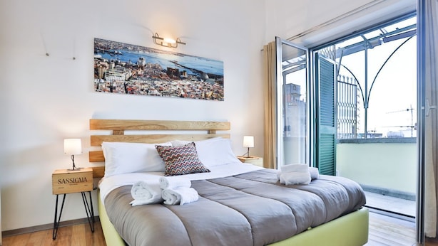 A modern bedroom with a large bed, a cityscape painting, a nightstand, and a view of the outside. - GuestHost - Terrace Concordia Amazing View (Napoli)