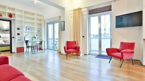 A spacious living area with a wooden floor, a red armchair, a sofa, a TV mounted on the wall, and a bookshelf. - GuestHost - Terrace Concordia Amazing View (Napoli)