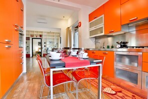 A modern kitchen with orange cabinetry, a dining table with chairs, and a visible clock.