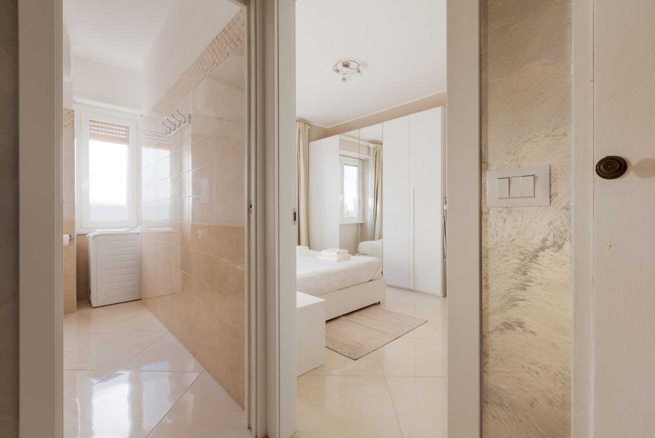 Un dormitorio moderno con cama, espejo y puerta que da a otra habitación.