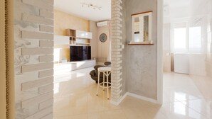 Una cocina moderna con horno integrado, un comedor con mesa redonda y dos sillas, y una sala de estar con sofá y televisor.