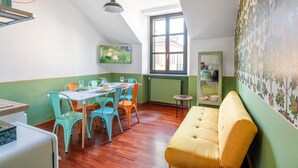 Ein Essbereich mit Tisch und Stühlen, einer Couch, einem Heizkörper, einem Fenster und einer Wand mit Blumenmuster.