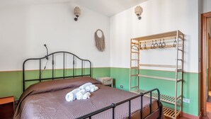 Ein Einzelbett mit Kopfteil, ein Holzregal mit Haken sowie eine Wandleuchte.