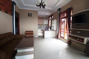 A modern living room with a sofa, a television, and a kitchen in the background.