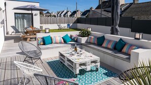 An outdoor patio with a white sofa set, a wooden table, and two chairs. - Au Gré du Vent by Interhome (Brignogan-Plage)